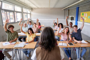 high school students raising hands to answer teacher's question in classroom.