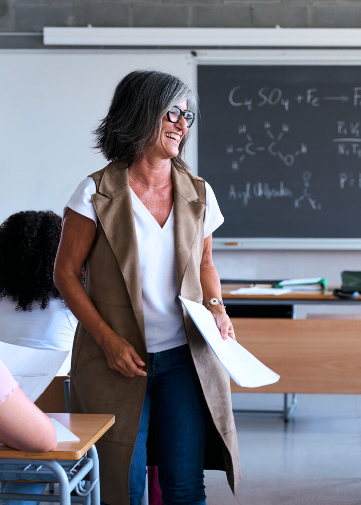 smiling teacher giving lecture to diverse high school students in classroom